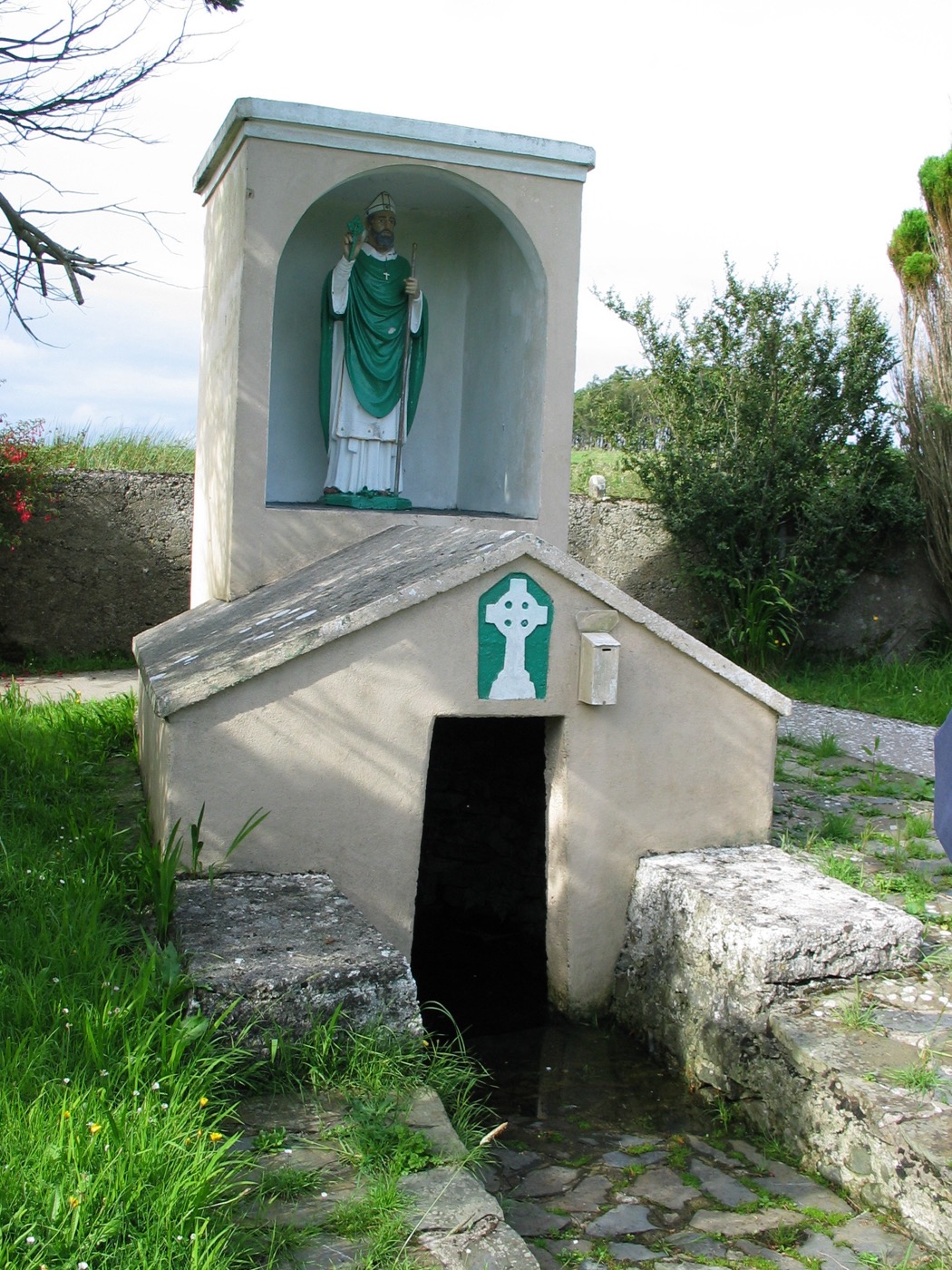 A white holy-well shrine with a statue of Saint Patrick above a small arched water opening.
