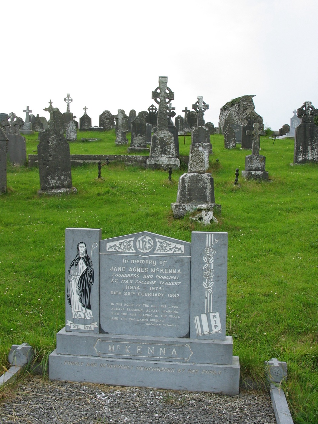 Jane Agnes McKenna memorial in a graveyard with Celtic-cross headstones and a ruined building behind it.